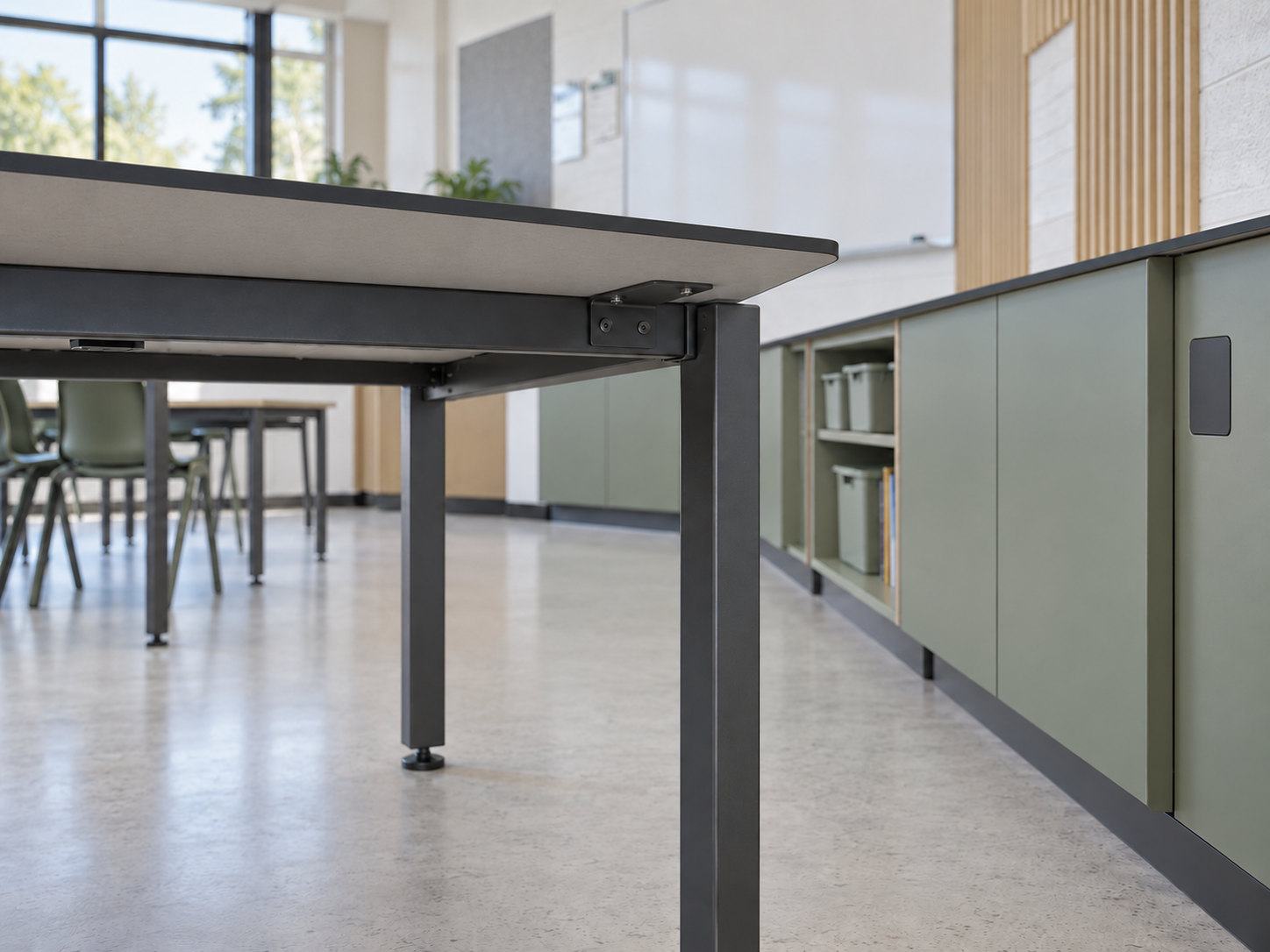Illustrative underside detail of a slim tabletop joined by a metal bracket to a support rail and square leg beside fitted cabinets.