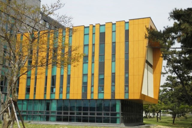 Building facade with vertical yellow screening elements and teal-colored glazing.