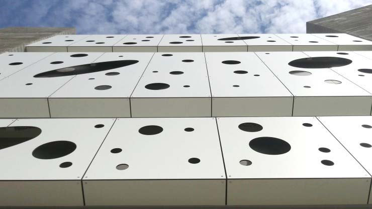 Close view of light-colored perforated facade panels with varied circular openings and visible module joints.