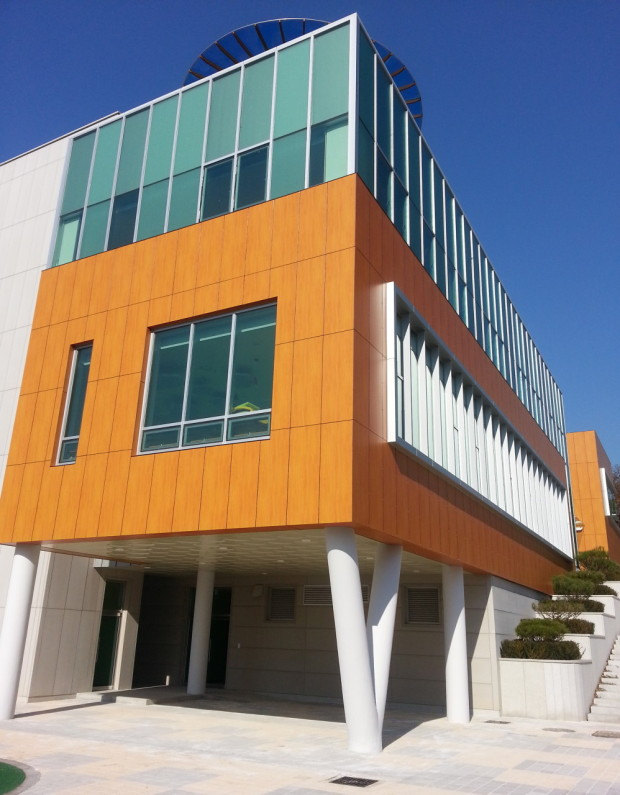 Elevated building with warm-colored exterior panels, glazing and supporting columns.