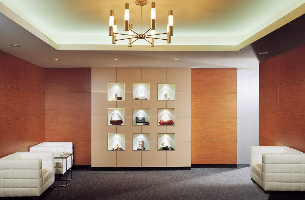 Retail lounge with warm wall panels, illuminated display niches, white seating and a recessed ceiling.