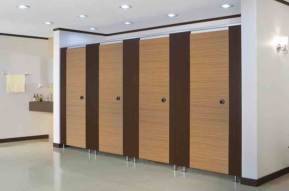 Washroom cubicle system with wood-tone doors and dark brown pilasters.