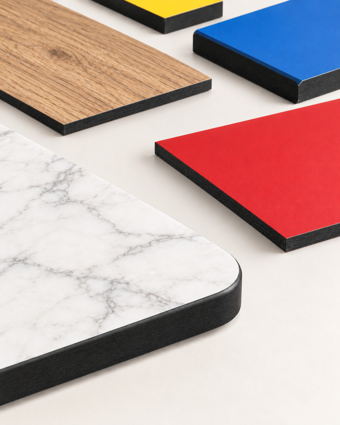 Compact laminate samples with solid colours, woodgrain and a marble pattern, showing exposed dark cores and varied edge profiles.