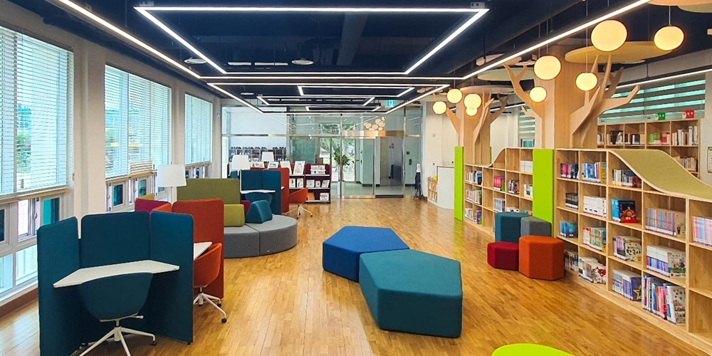 School reading space with small study tabletops beside windows, seating and bookshelves