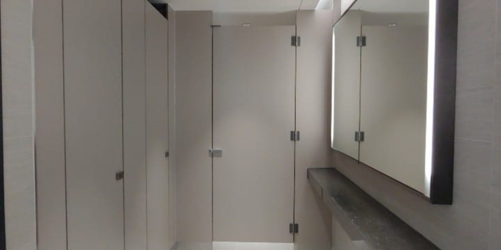 Light-coloured cubicle doors and partitions beside an office washroom basin and mirror