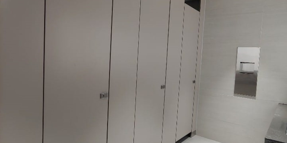 Office washroom cubicle doors with small locks beside a tiled wall and recessed dispenser
