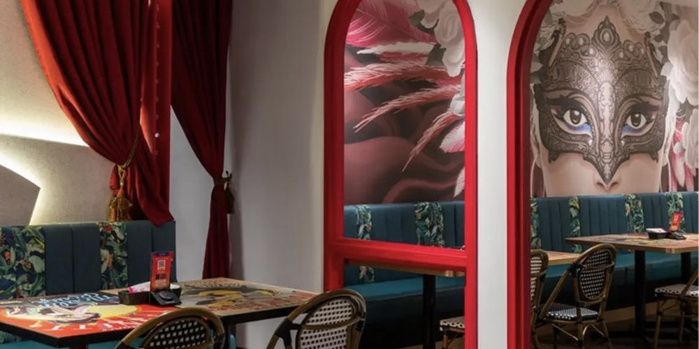Restaurant seating area with graphic tabletops, red frames and a masked-face wall image