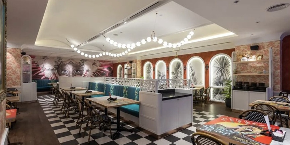 Restaurant tables and banquette seating viewed toward framed wall imagery
