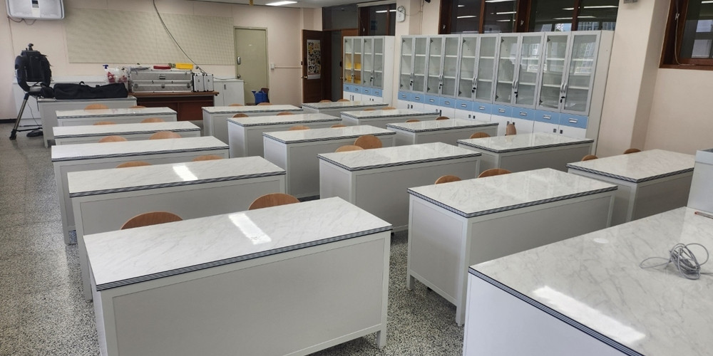 Rows of school laboratory tables with pale patterned worktops and exposed panel edges